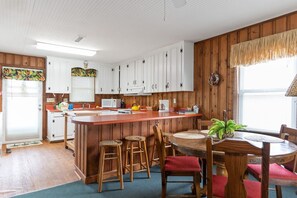 Una cocina con armarios blancos, una isla de madera y un comedor con sillas y mesa de madera.