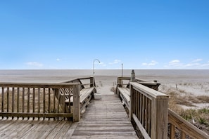 Un muelle de madera que lleva a una playa con cielo despejado.