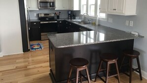 A modern kitchen with white cabinets, a granite island, and a stainless steel refrigerator. - Best Day Ever 4 Bedroom Home by RedAwning (Supply)