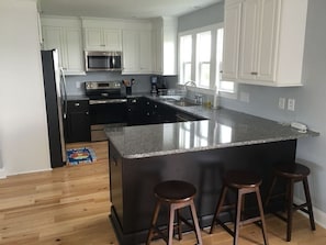 A modern kitchen with white cabinets, a granite island, and a stainless steel refrigerator.