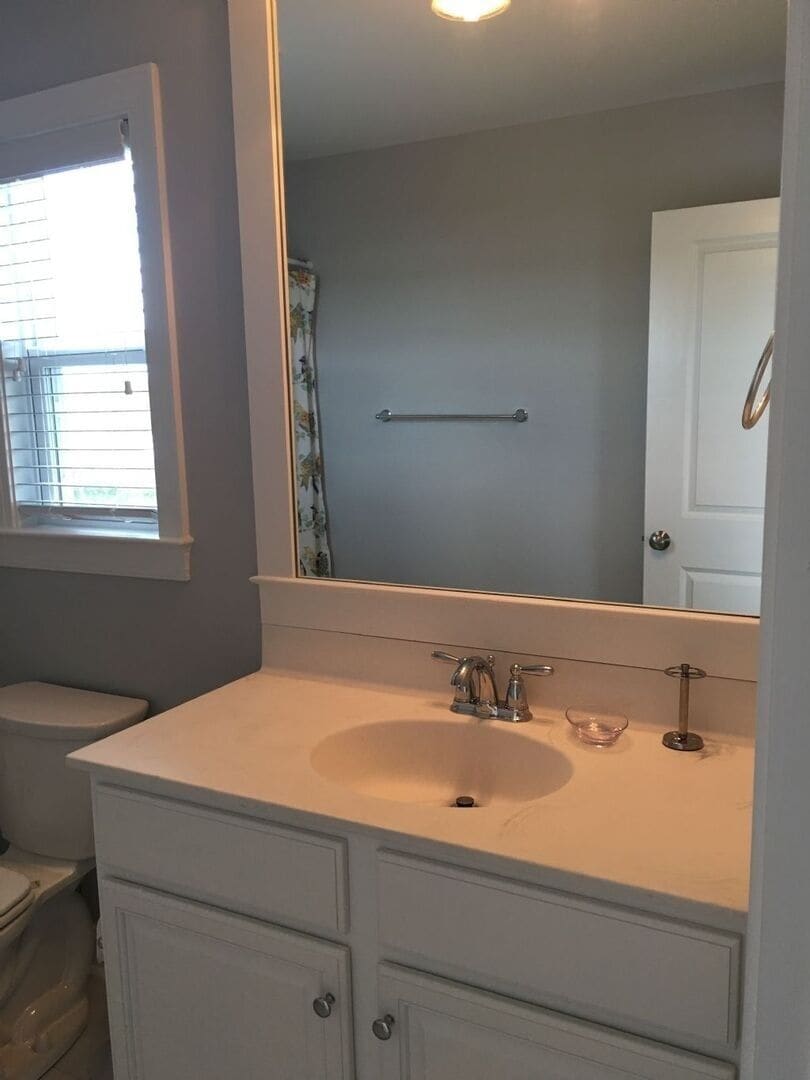 Un baño con lavamanos blanco, espejo y retrete.