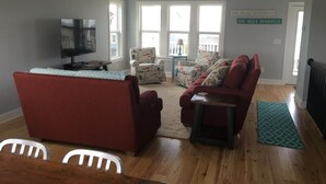 A living room with a red sofa, a television, and a ceiling fan. - Best Day Ever 4 Bedroom Home by RedAwning (Supply)