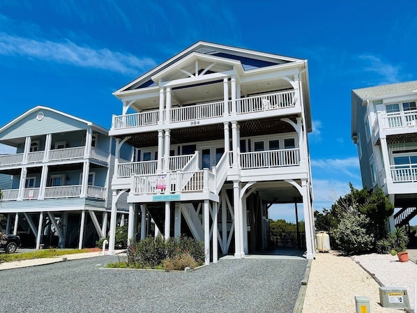 A multi-story beachfront property with a balcony, a covered entrance, and a clear sky.