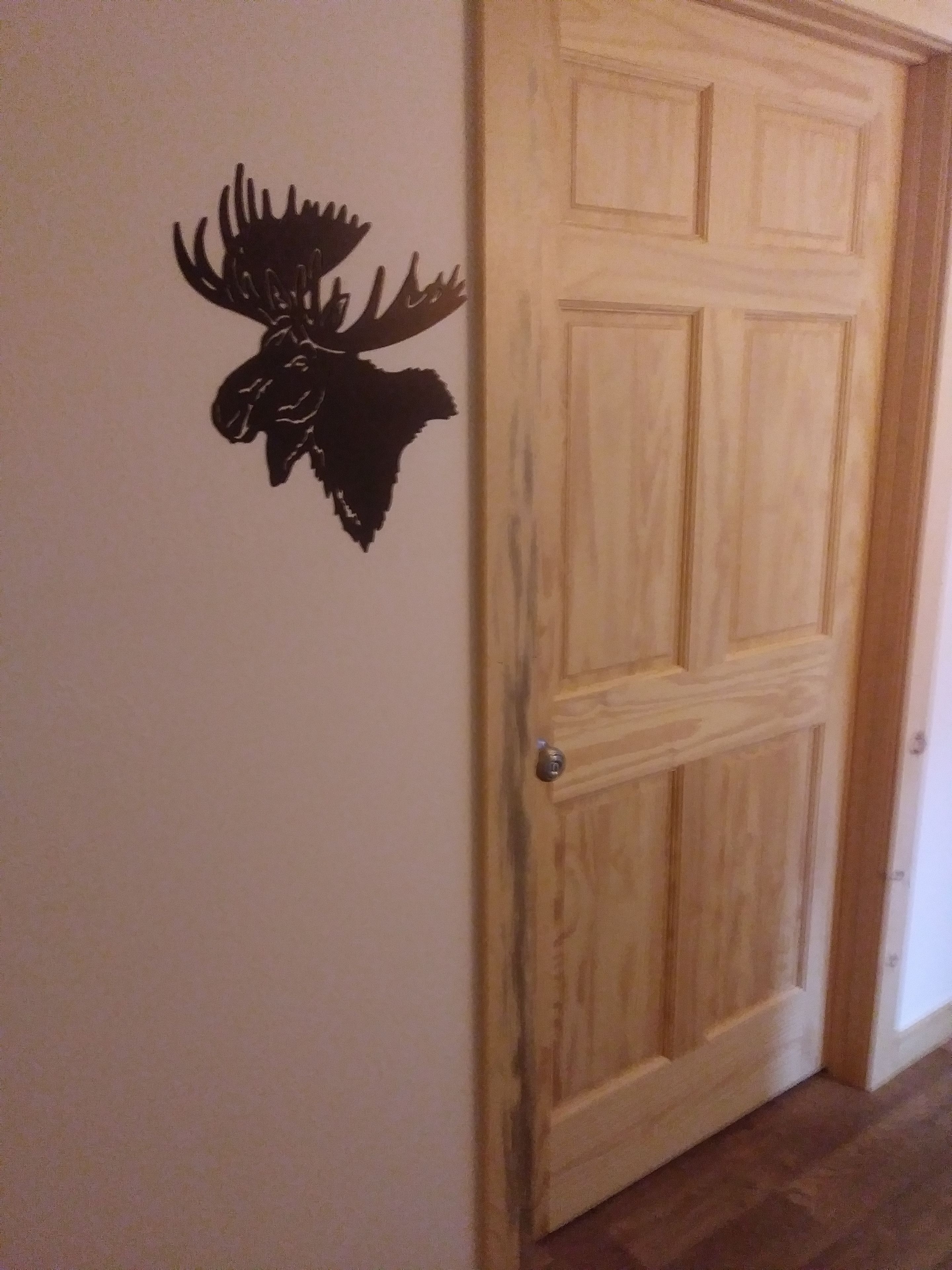 A wooden door with a keyhole and a wall decal of a moose head.