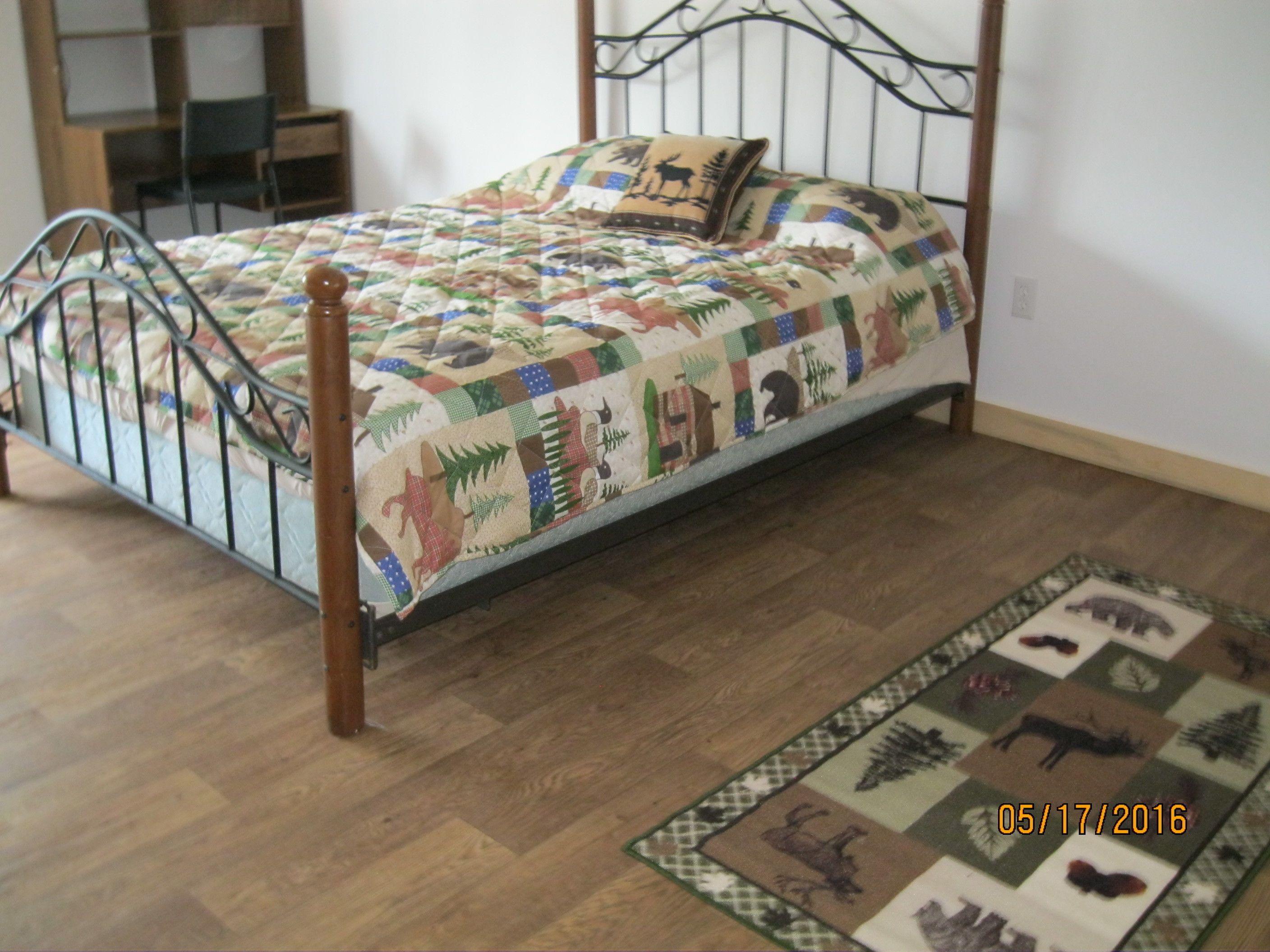 Una cama con colcha estampada con motivos animales, cabecera de madera y una pequeña alfombra con diseños de animales en el suelo.