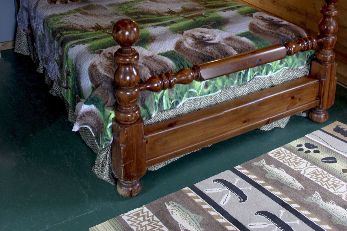 A wooden bed with a green and brown patterned bedspread, a nightstand with a lamp, and a framed picture of a whale tail on the wall.