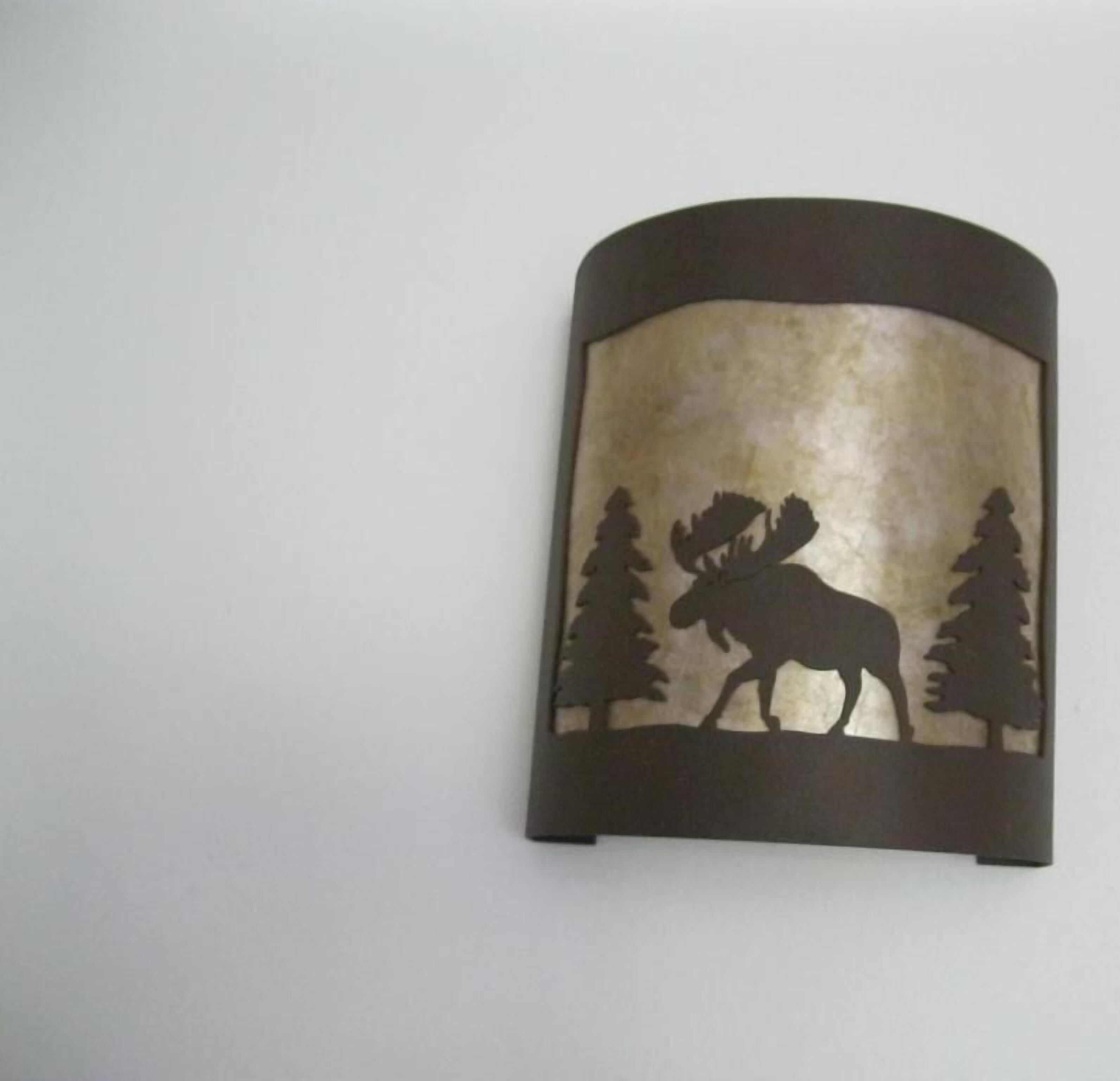 A wall-mounted light fixture with a silhouette of a moose and trees.