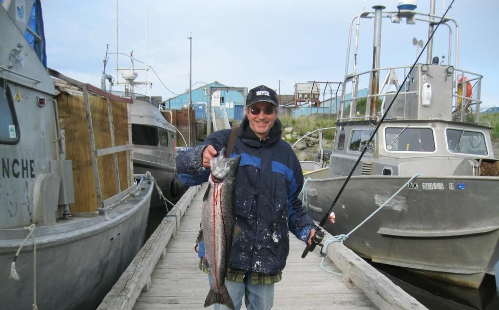 A dock with boats, a person holding a fish, and a building in the background.