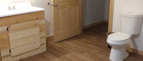 A bathroom with a wooden vanity, a toilet, and a door leading to another room.