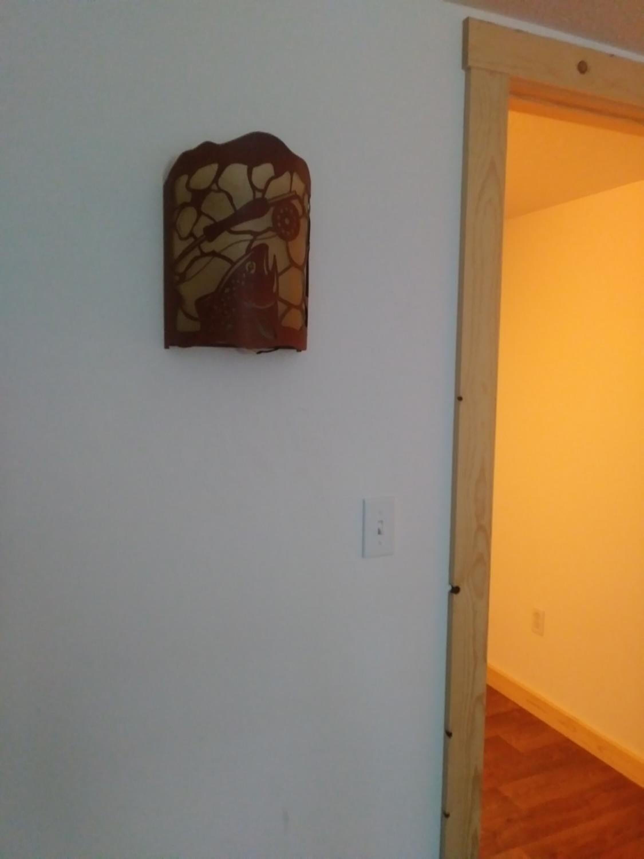 Una habitación con una puerta de madera que da a otro espacio, un interruptor de luz instalado en la pared y un adorno en la pared.