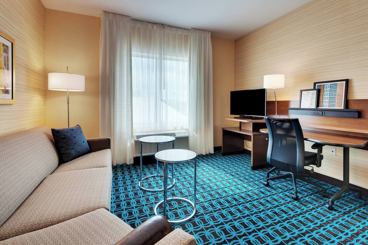 A hotel room with a sofa, a desk, a chair, a TV, and a small table.