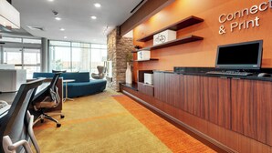 Un espace d’accueil moderne avec un comptoir de réception en bois, un téléviseur fixé au mur et un panneau indiquant « Connectez-vous et imprimez ».