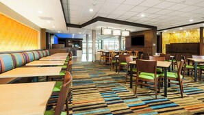 Un hall d’hôtel avec une longue rangée de tables et de chaises, une moquette à motifs et un grand mur orné d’un décor texturé.