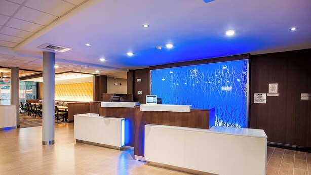 Un espace d’accueil d’hôtel au design moderne, comprenant un comptoir d’accueil, un coin salon et une grande fenêtre donnant sur des arbres sans feuilles.