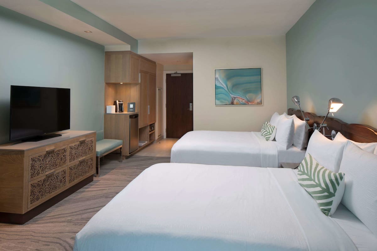A hotel room with two beds, a TV, a wooden cabinet, and a painting on the wall.