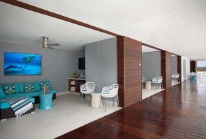 A modern living room with a teal sofa, white chairs, and a ceiling fan.