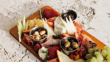 Uma tábua de frios com diversos queijos, carnes, frutas e nozes sobre uma base de madeira.