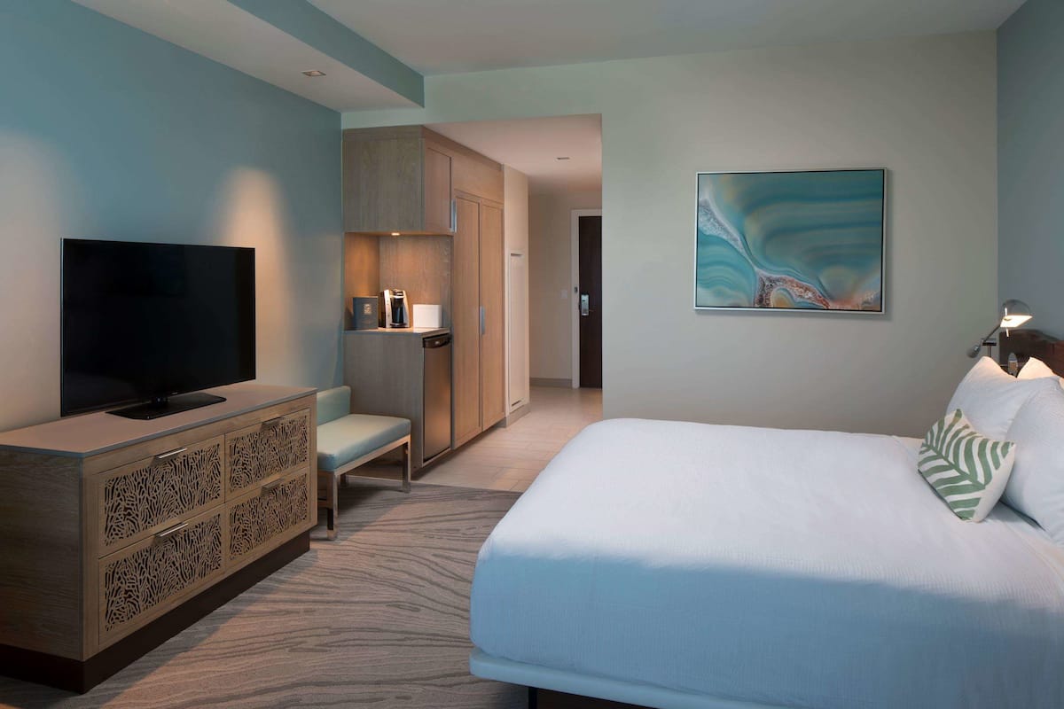 A hotel room with a large bed, a television, a wardrobe, a bench, and a painting on the wall.