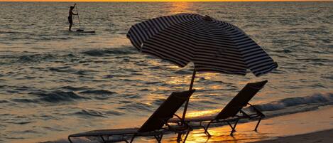 A beach with two sun loungers and a striped umbrella.