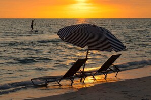 A beach with two sun loungers and a striped umbrella.