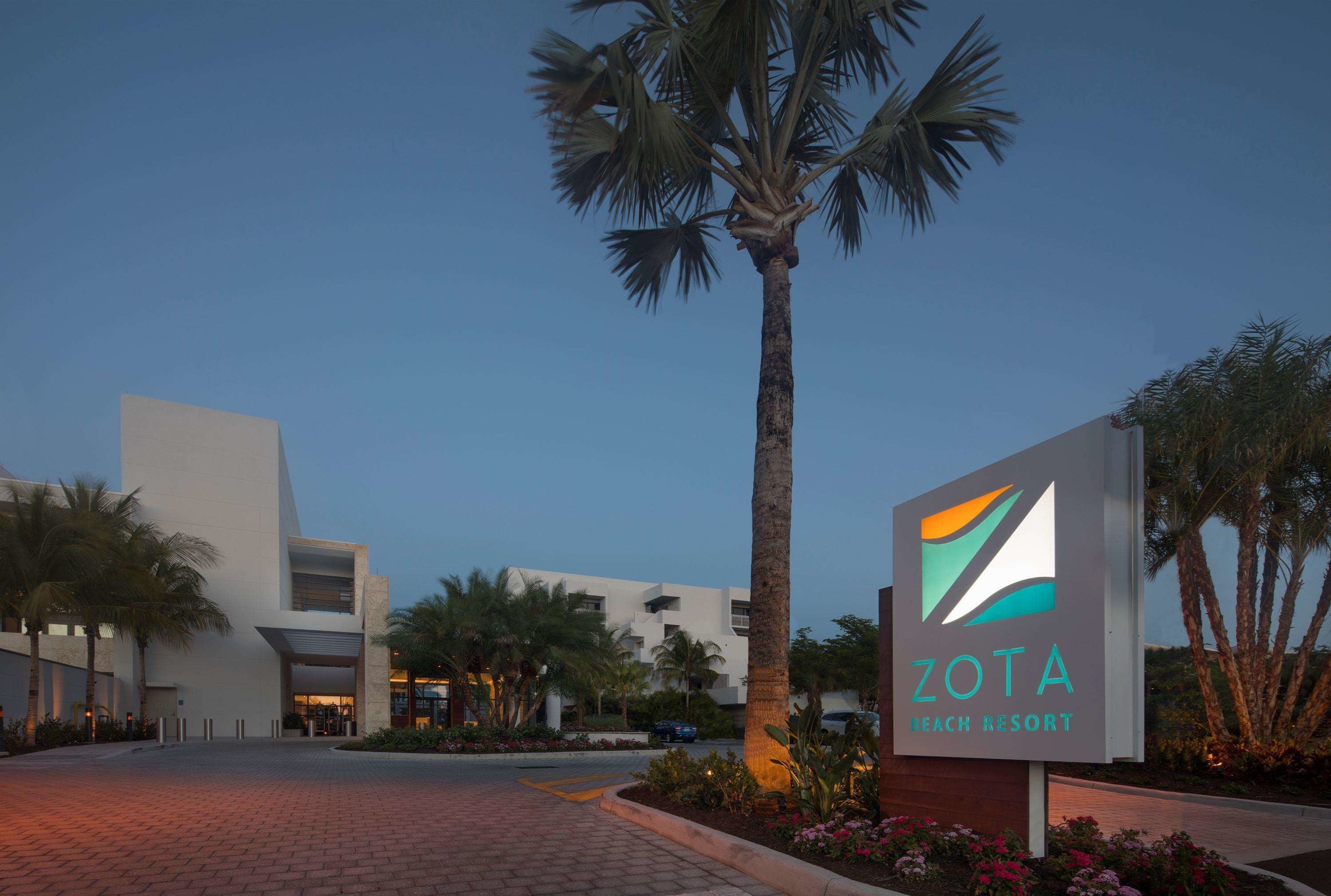 A sign for Zota Beach Resort with a modern building in the background.