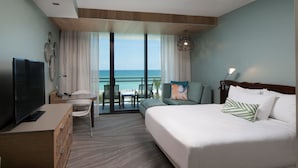 A hotel room with a large bed, a desk with a TV, a balcony with a view of the ocean, and a seating area with a table and chairs. - Zota Beach Resort (Longboat Key)