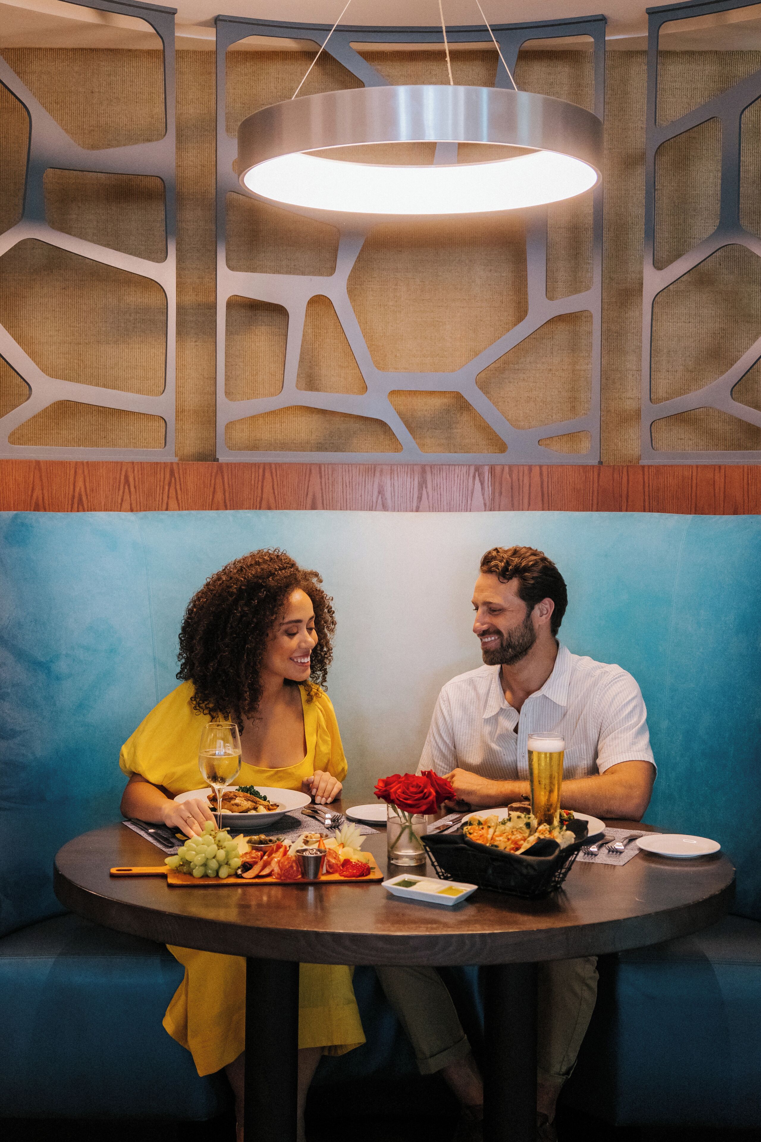 A couple dining at a round table with a modern chandelier overhead.