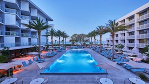 A pool area with lounge chairs and umbrellas, surrounded by palm trees and a building with balconies. - Zota Beach Resort (Longboat Key)