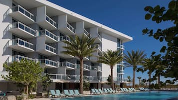 A modern hotel with multiple balconies, a swimming pool, and palm trees.