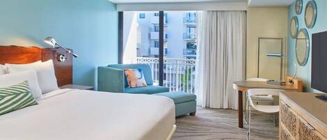 Quarto de hotel com uma cama grande, um sofá pequeno, uma escrivaninha e uma varanda com vista para edifícios.