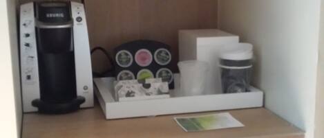 Una kitchenette con cafetera, un refrigerador pequeño y un dispensador para cápsulas de café.