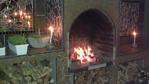 Een haard met brandende blokken hout, omringd door een stenen muur en een metalen hekwerk.