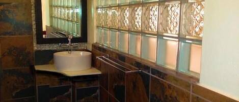 Un baño con lavamanos de mármol, un espejo y paneles de vidrio decorativos.