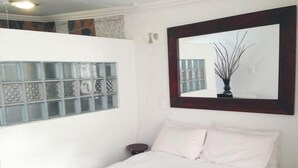 Een slaapkamer met een bed, een nachtkastje, een spiegel en een raam met decoratieve glaspanelen.