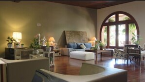 A spacious living room with a wooden floor, a sofa, a coffee table, and a dining area with a table and chairs. - Hotel Mantovani (Águas de Lindóia)