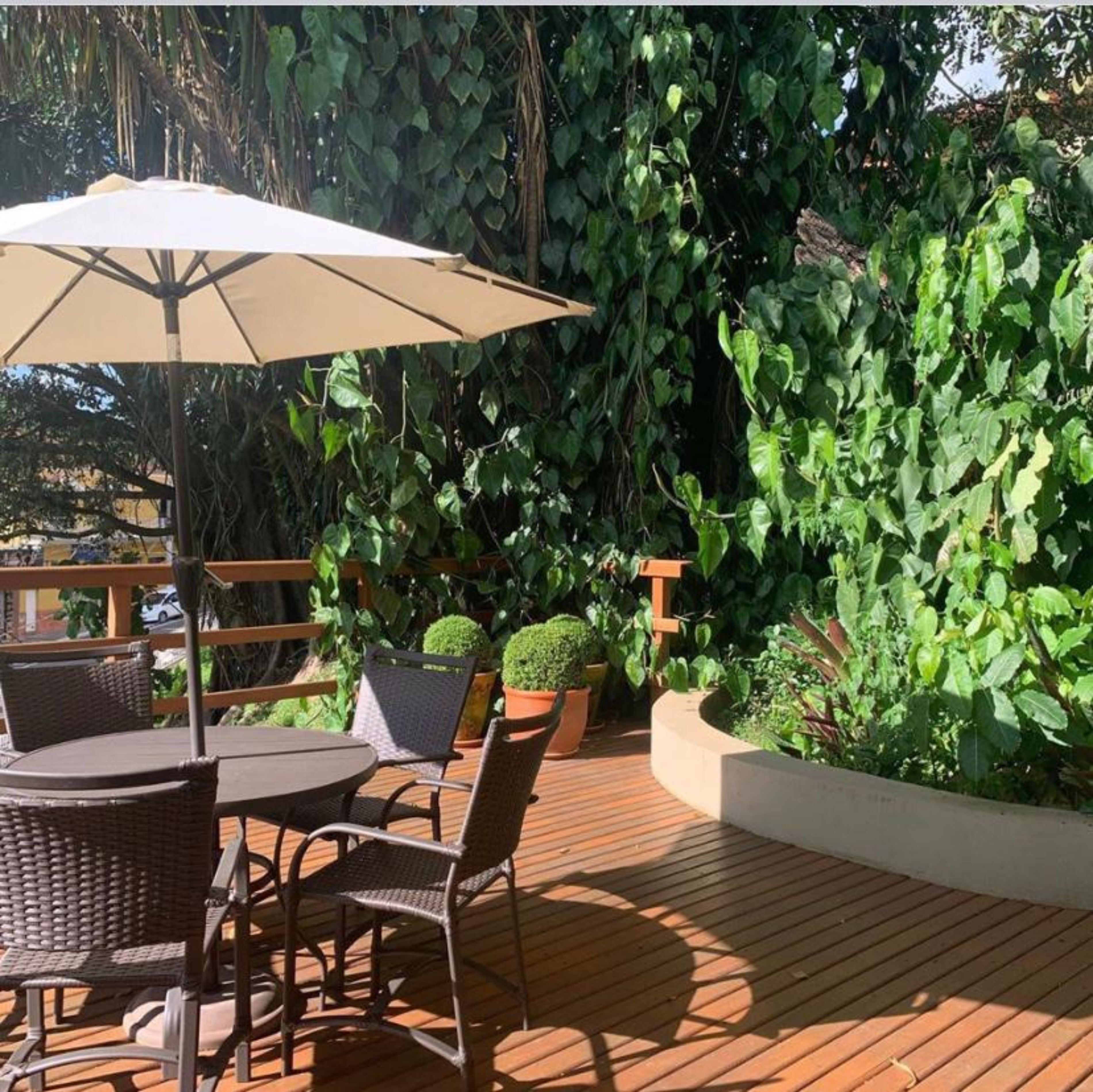 An outdoor patio with a round table and chairs, surrounded by lush greenery and a wooden deck.