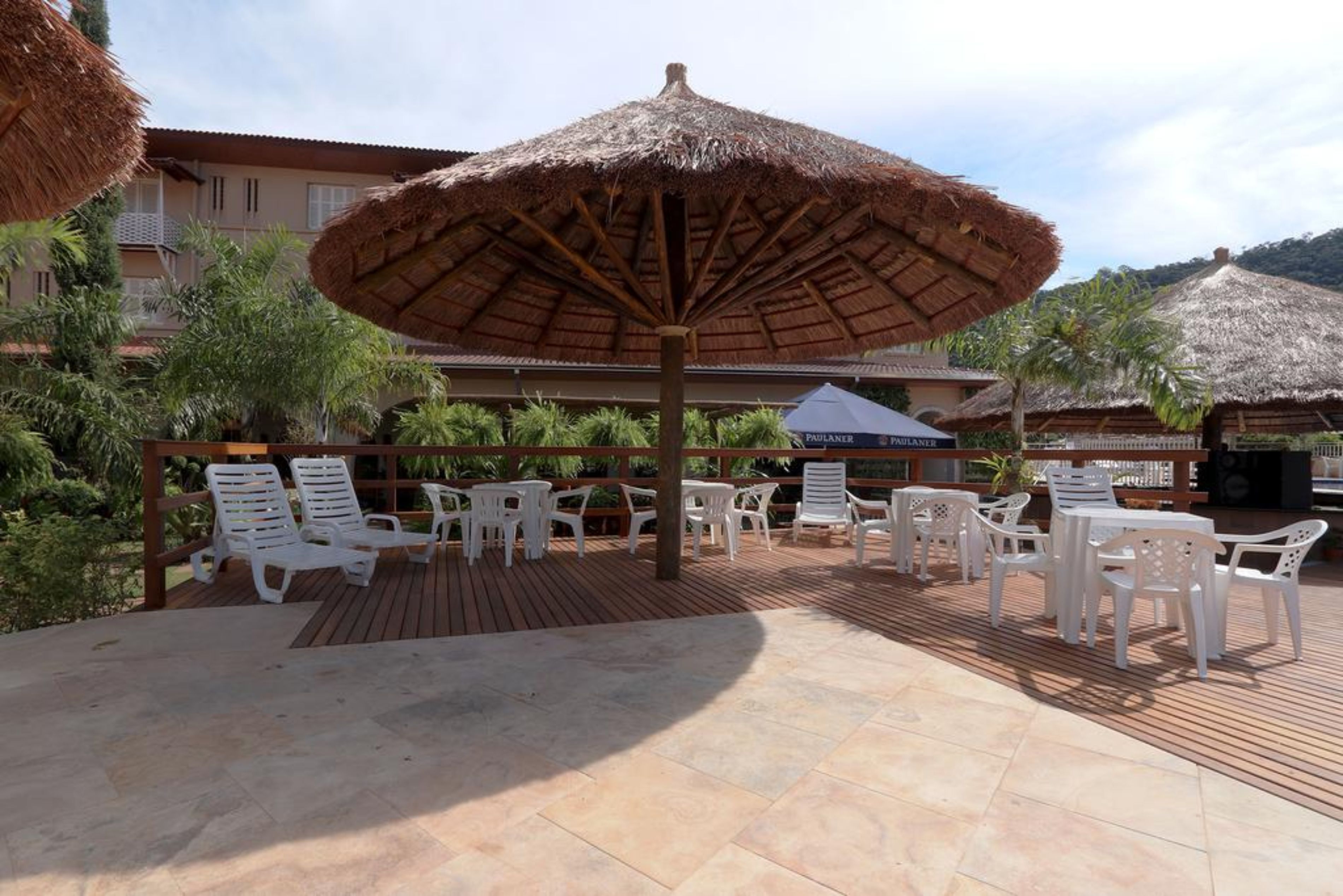 An outdoor patio with white plastic chairs and tables, a thatched umbrella, and a wooden deck.
