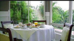 A dining table set with plates, cups, and a glass of orange juice, surrounded by chairs with a view of lush greenery outside. - Hotel Mantovani (Águas de Lindóia)