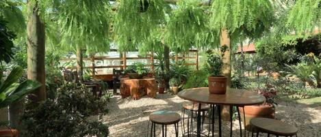 An outdoor seating area with a round table and four stools, surrounded by potted plants and a wooden pergola.