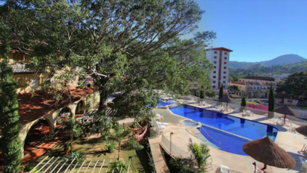 A resort with a large swimming pool, lush greenery, and a mountain backdrop. - Hotel Mantovani (Águas de Lindóia)