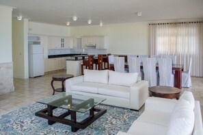 A modern living room with a white sofa, a glass coffee table, and a dining area with chairs and a table. - OceanFront Condo E-3 at Los Balcones (Sosúa)