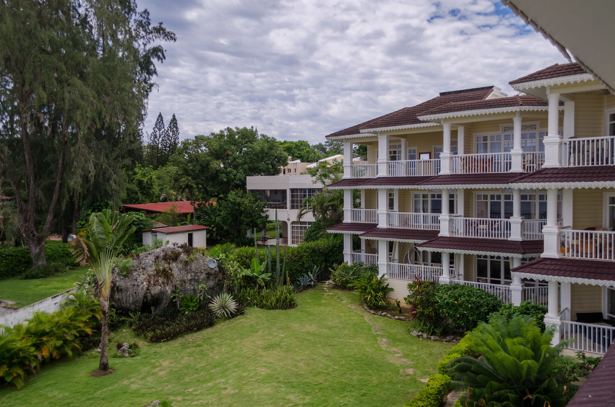 A multi-story hotel with balconies, surrounded by lush greenery and a well-maintained lawn.