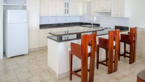 Una cocina con armarios blancos, encimera de granito y sillas de madera.