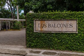 A sign reading "LOS BALCONES" against a backdrop of lush greenery and a covered structure. - OceanFront Condo E-3 at Los Balcones (Sosúa)