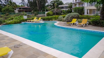 A swimming pool with clear blue water, surrounded by stone tiles and yellow lounge chairs.