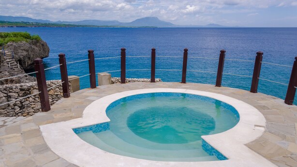 Una piscina con terraza de piedra y vista al mar.