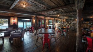 Un interior rústico con pisos de madera, sillas rojas y grises, y una zona de bar.