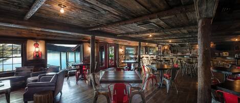 Un interno rustico con pavimenti in legno, sedie rosse e grigie e un angolo bar.