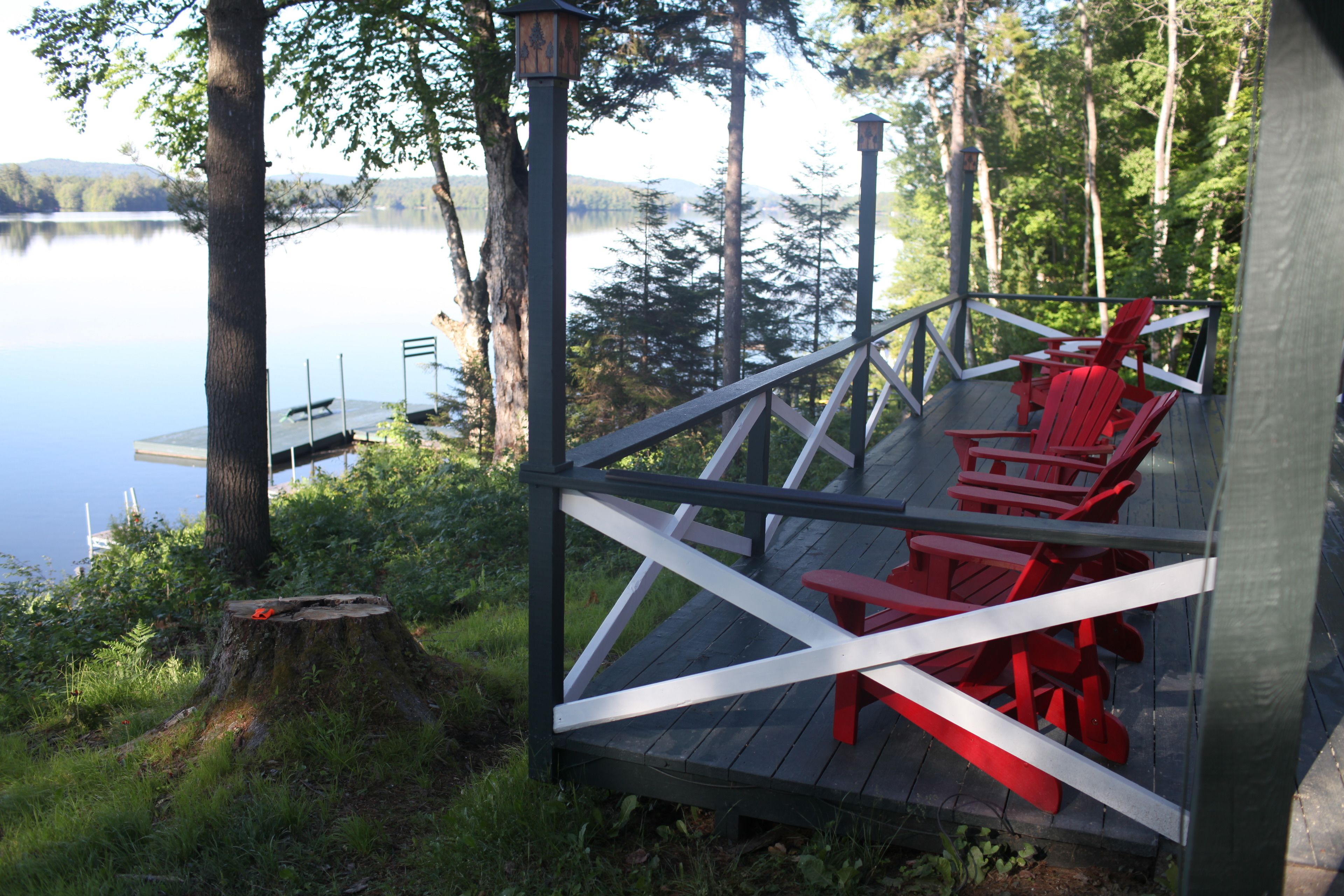 A wooden deck with red chairs and a table overlooking a lake.
