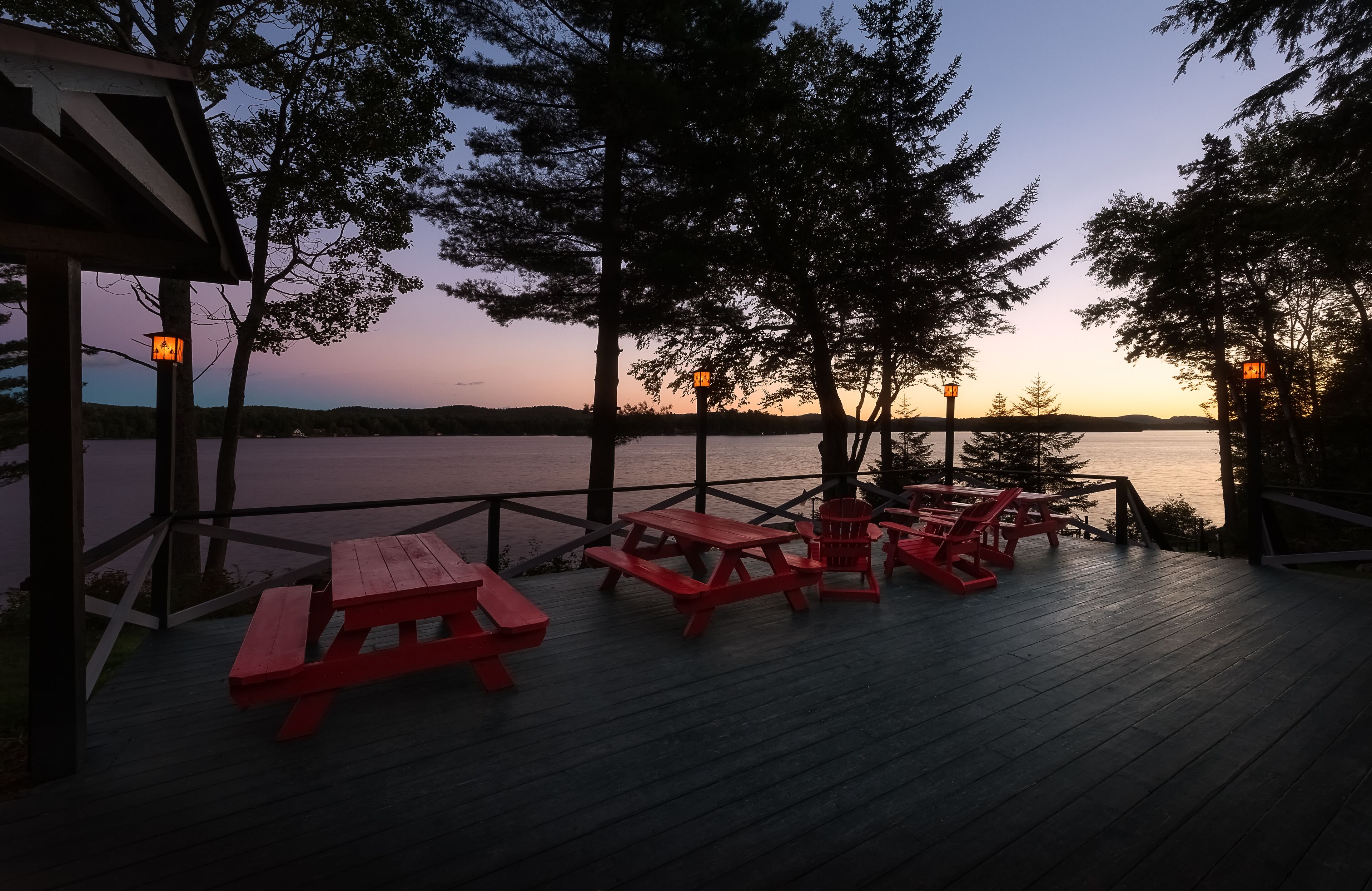 A wooden deck with picnic tables and benches overlooking a body of water at dusk.